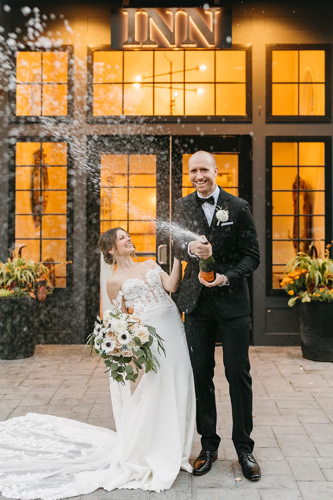 bride and groom pop champagne in front of inn