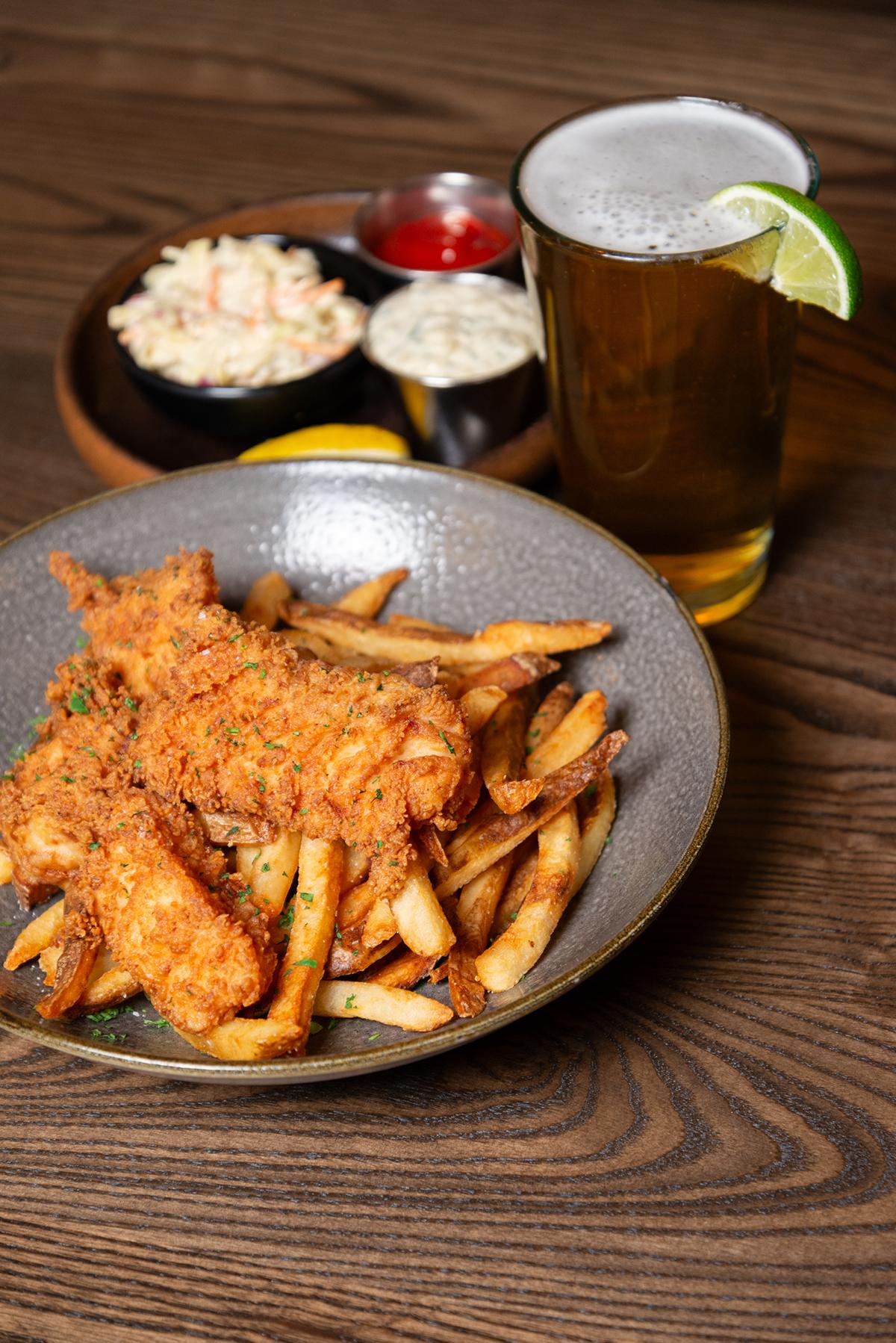 Fried fish and fries on a plate, with coleslaw and a beer with lime.