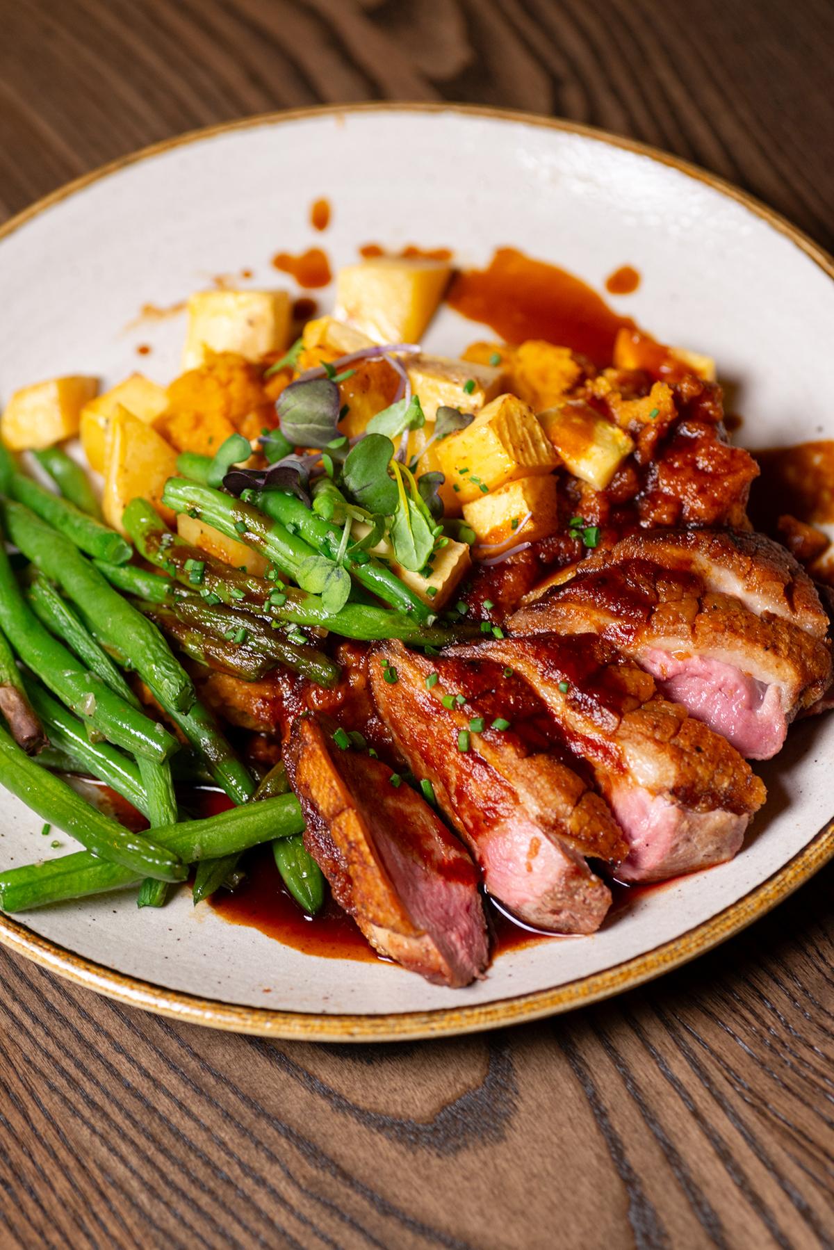 Sliced duck with green beans, potatoes, and sauce on a plate.