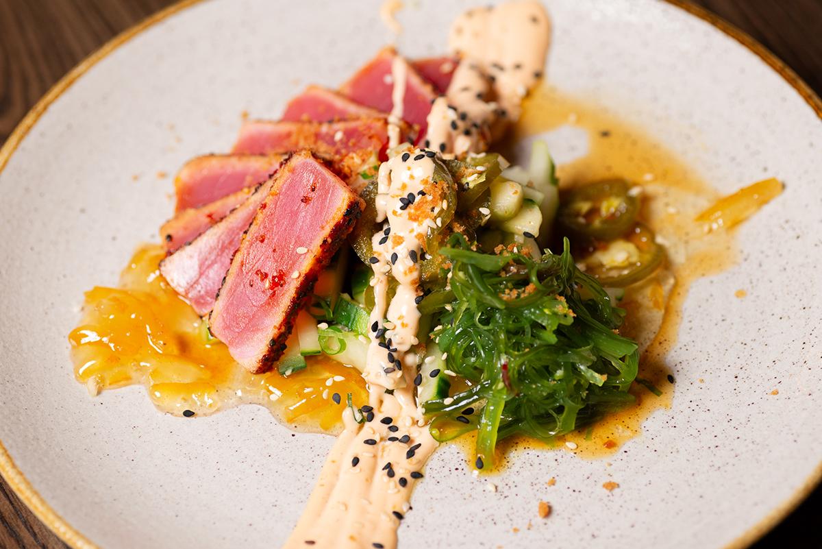 Seared tuna slices with seaweed salad and sauce on a plate.