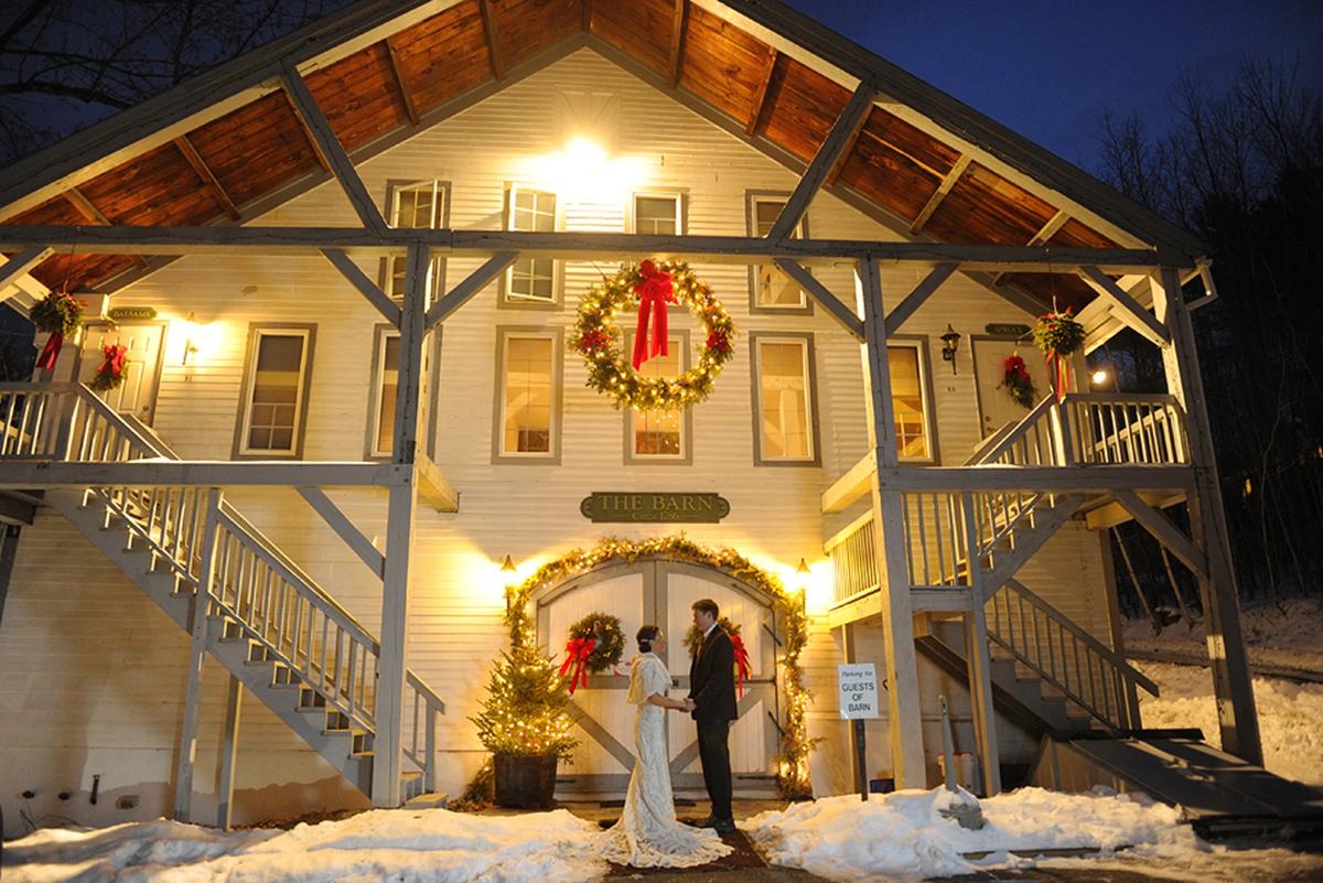 Couple in wedding attire under festive lights in front of a large, decorated house.