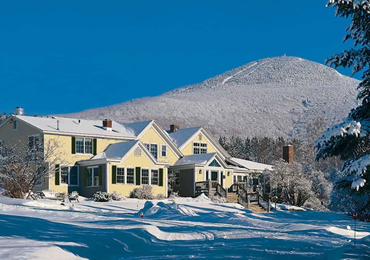 Yellow house in snowy landscape with mountain and clear blue sky.