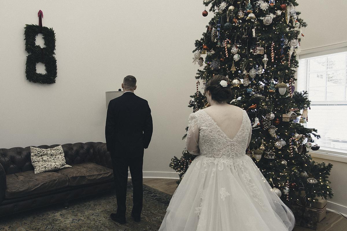 Bride and groom by a Christmas tree in a cozy living room.