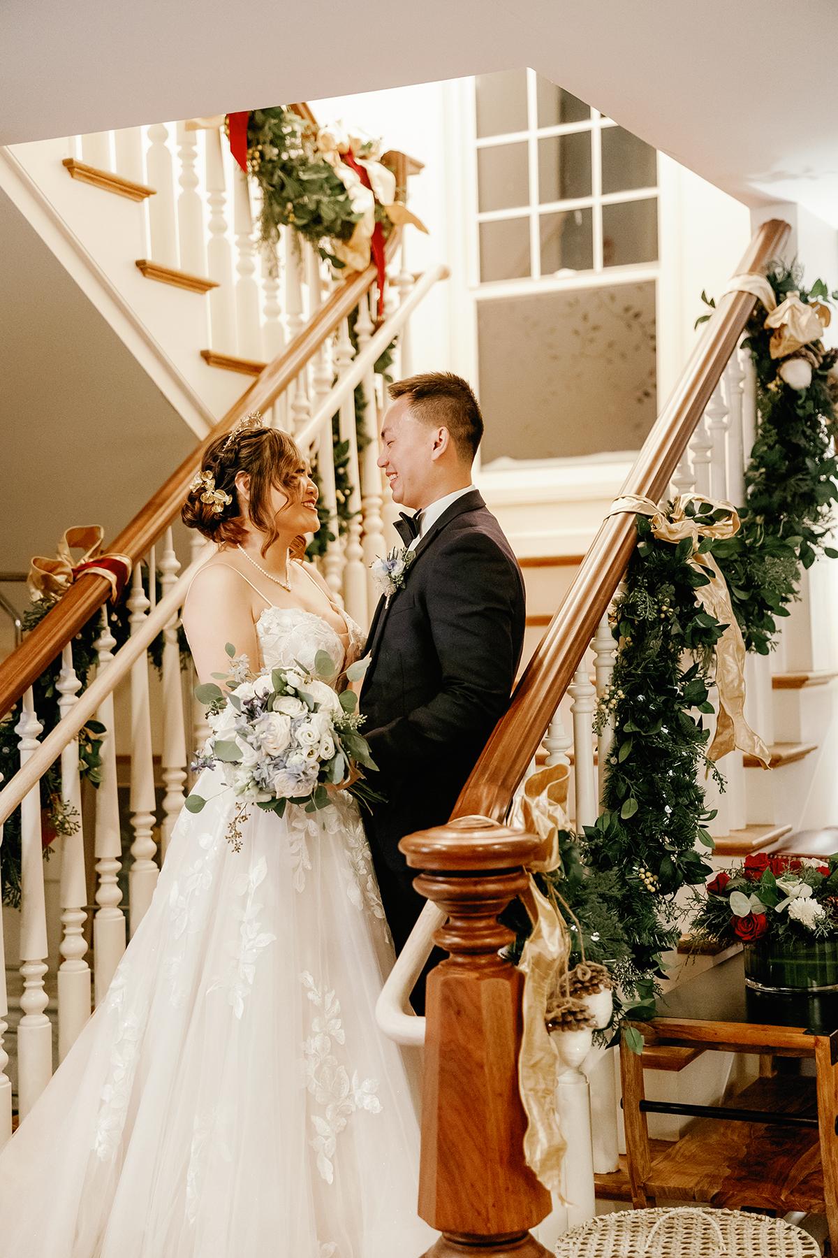 Bride and groom standing on a decorated staircase, holding hands.