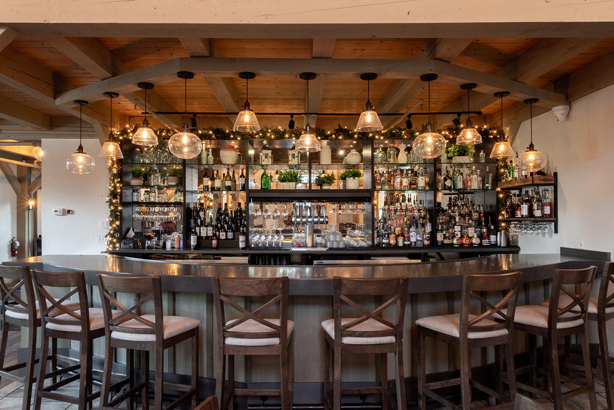 Cozy bar with hanging lights, wooden stools, and a stocked back shelf.