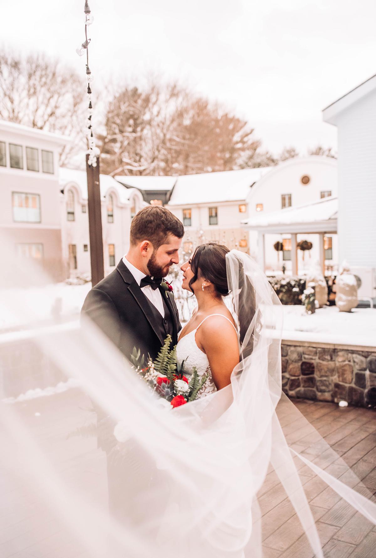 Bride and groom embracing outside, surrounded by snowy buildings.