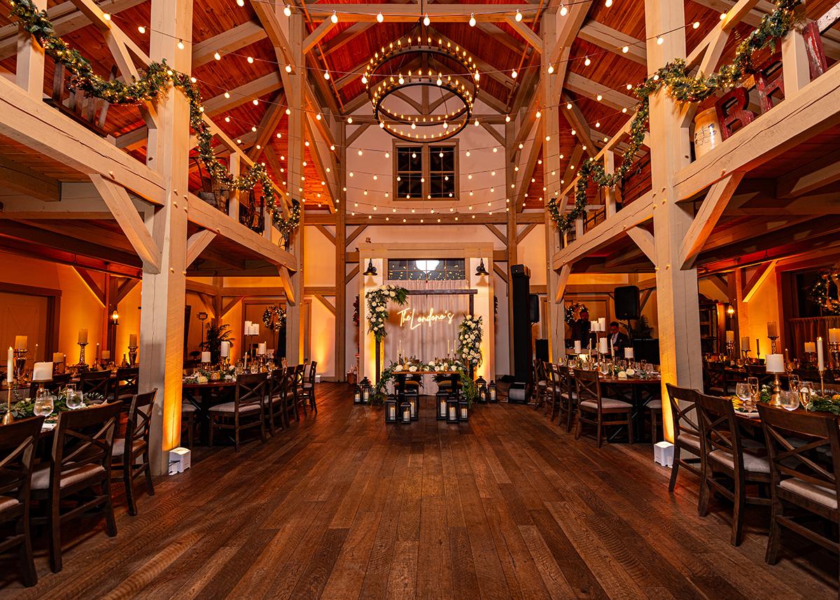 Rustic wedding venue with wooden beams, warm lights, and decorated tables.