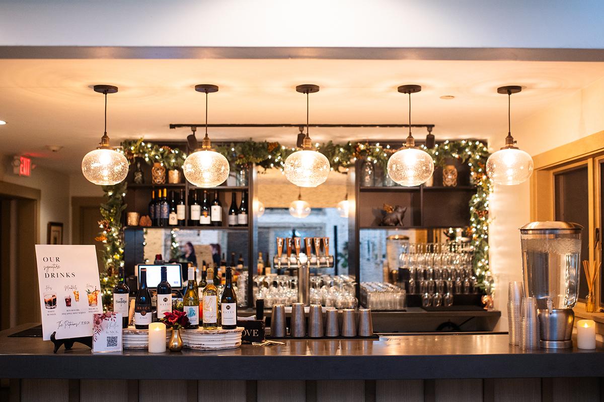 A warmly lit indoor bar decorated with foliage and lights.