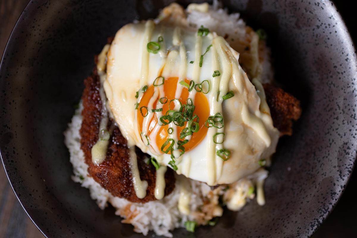 Rice bowl with a fried egg, sauce drizzle, and green garnish on top.