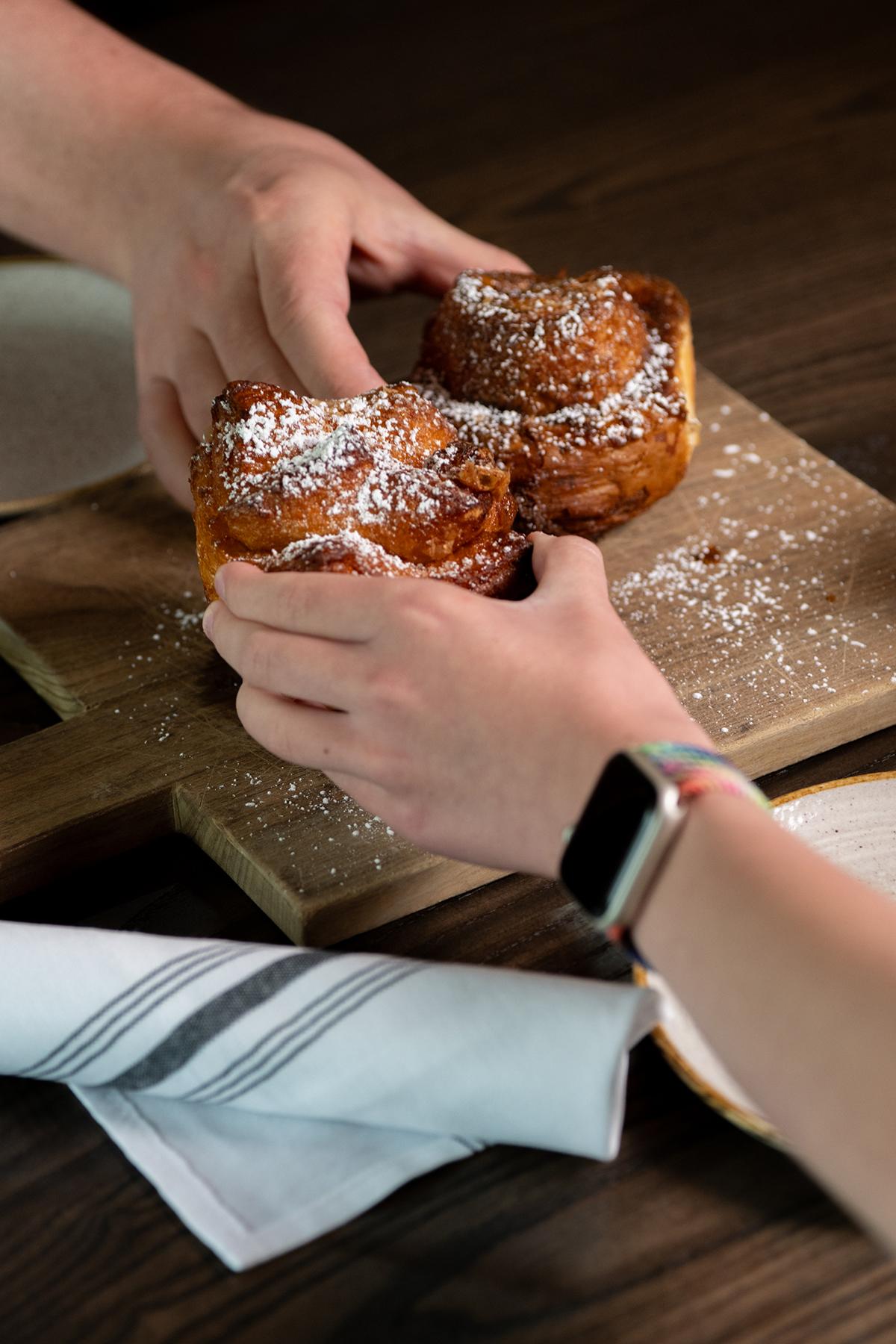 Two hands holding pastries dusted with powdered sugar on a wooden board.