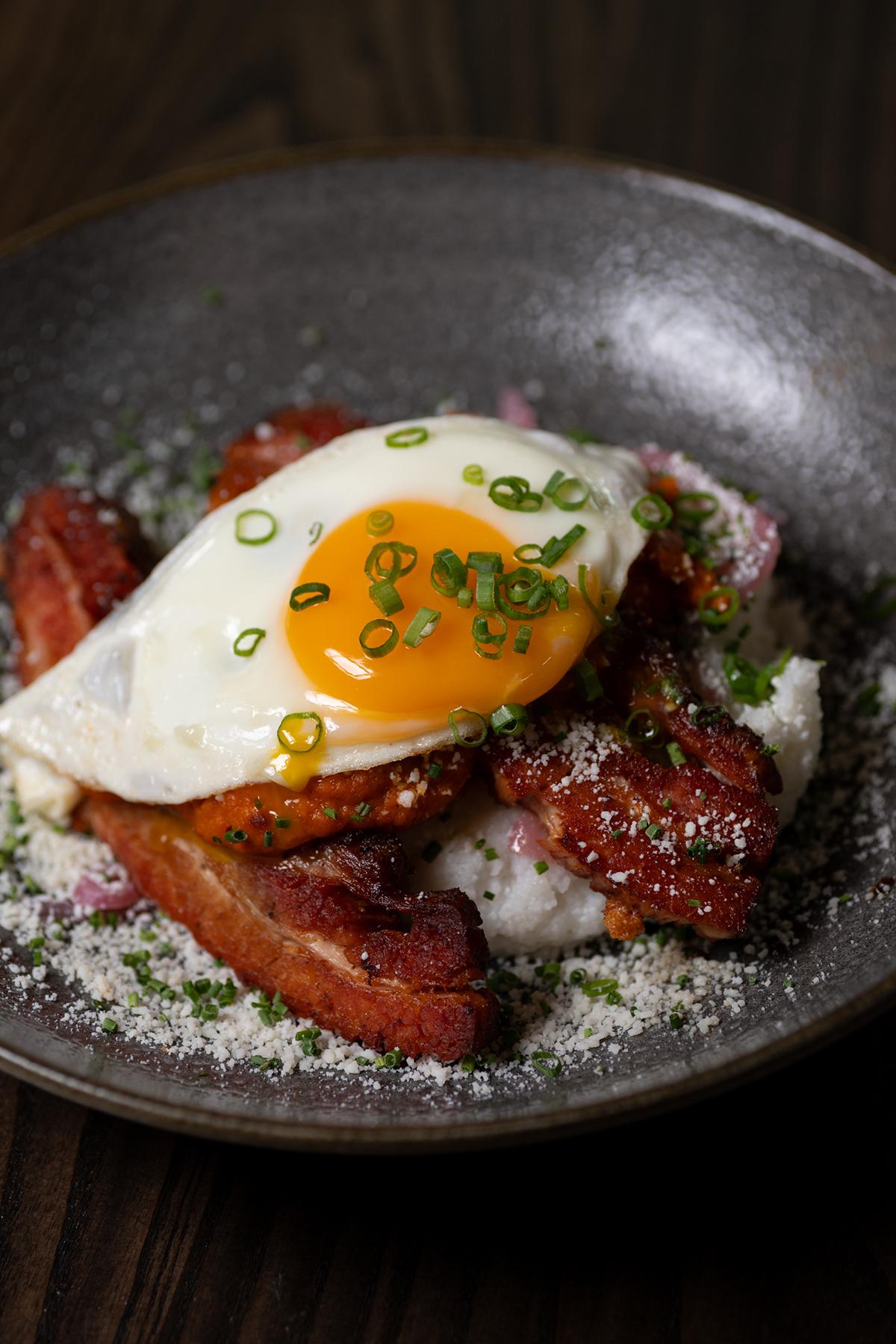 Fried egg on top of bacon with green onions on a dark plate.