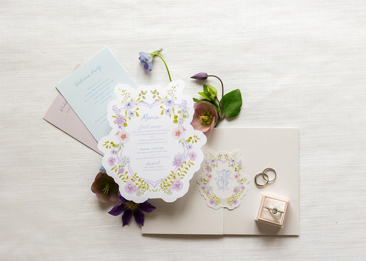 Wedding invitation set with floral designs, rings, and leaves on a light background.