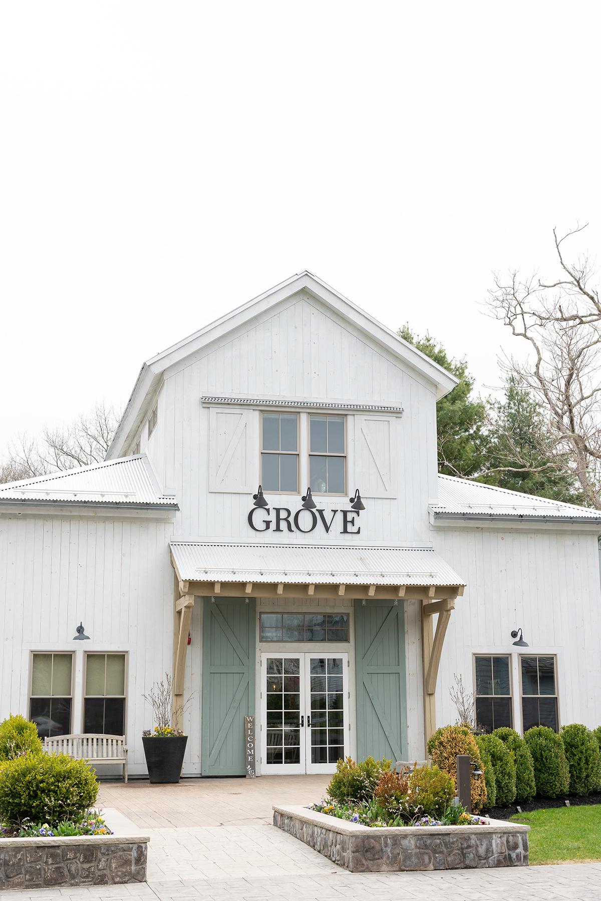 White barn-like building with green doors, surrounded by greenery.