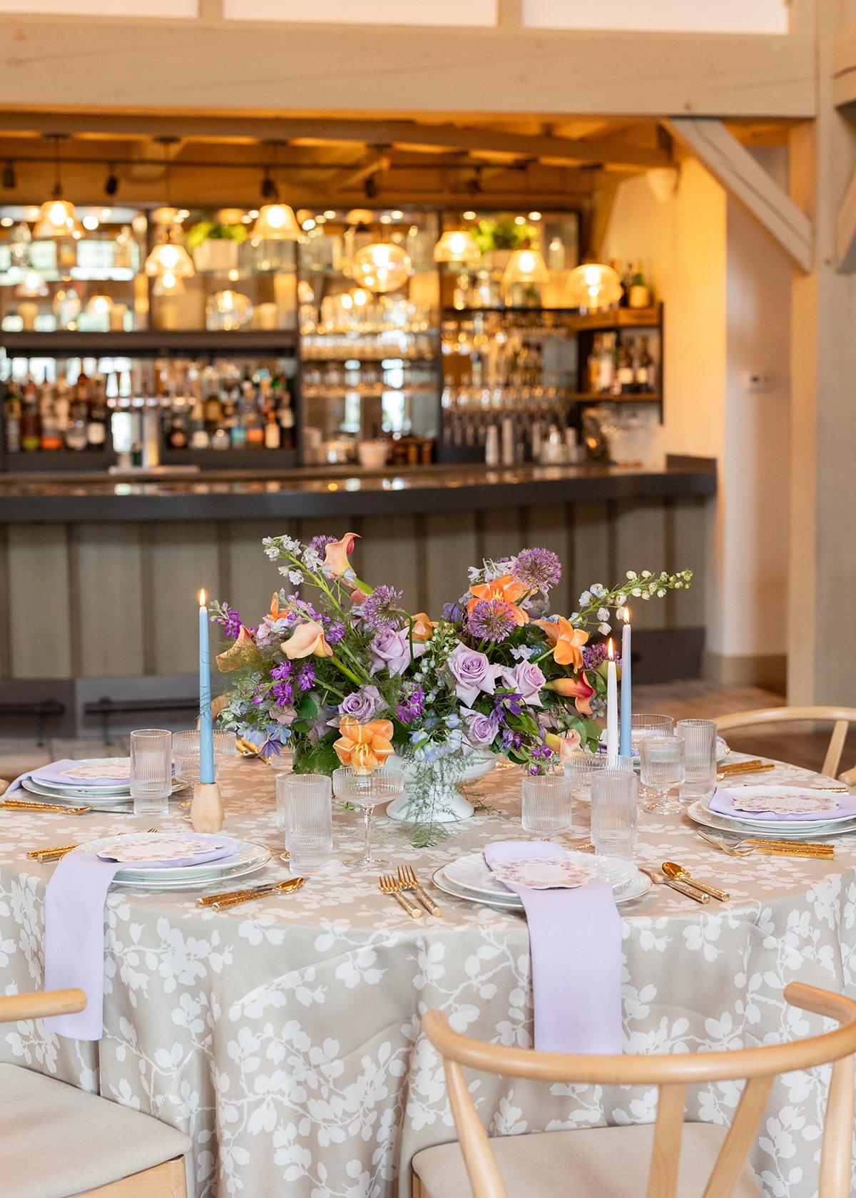 Elegant table setting with flowers and candles, bar in the background.