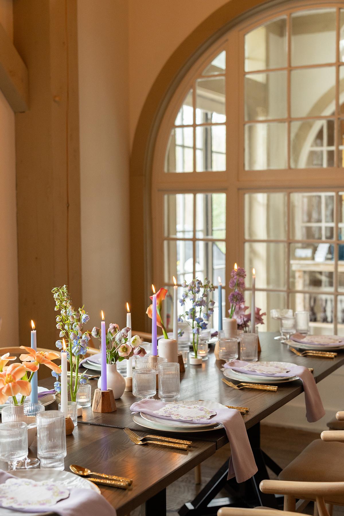 Elegant table setting with candles and flowers by a large arched window.