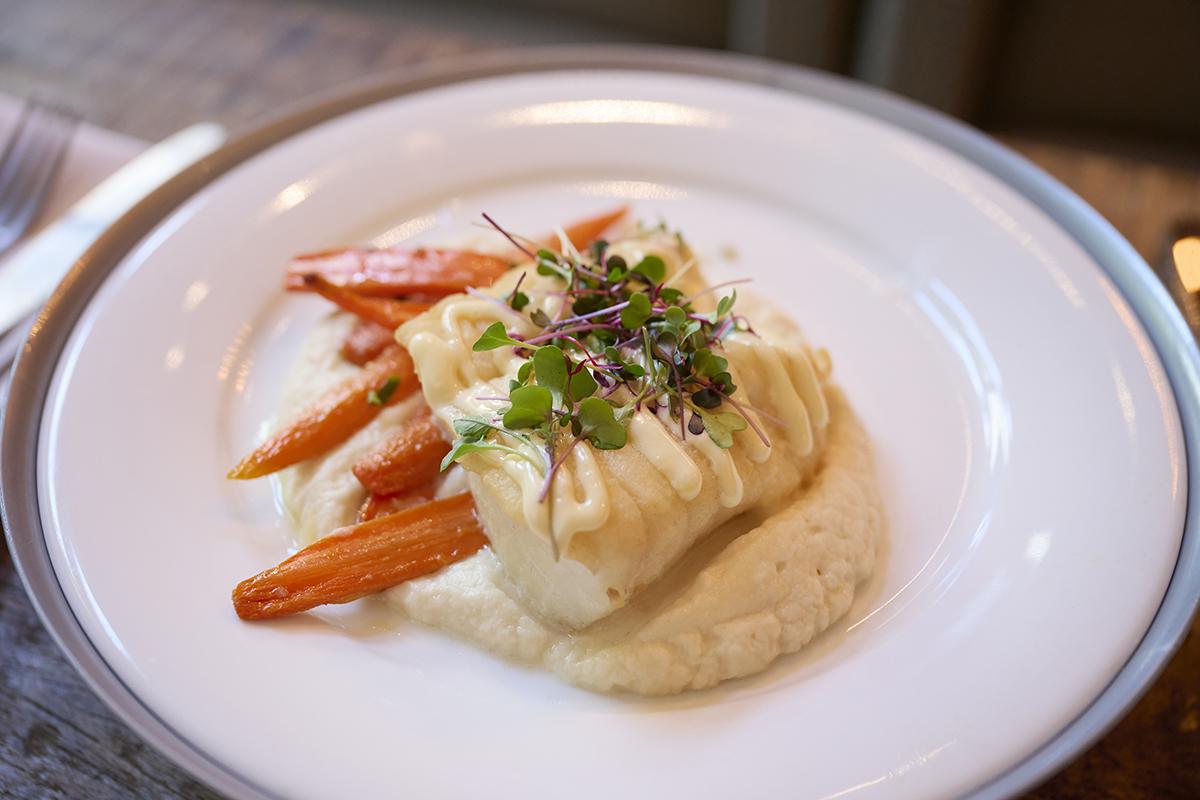 Seared fish with carrots on mashed potatoes, garnished with greens, on a white plate.