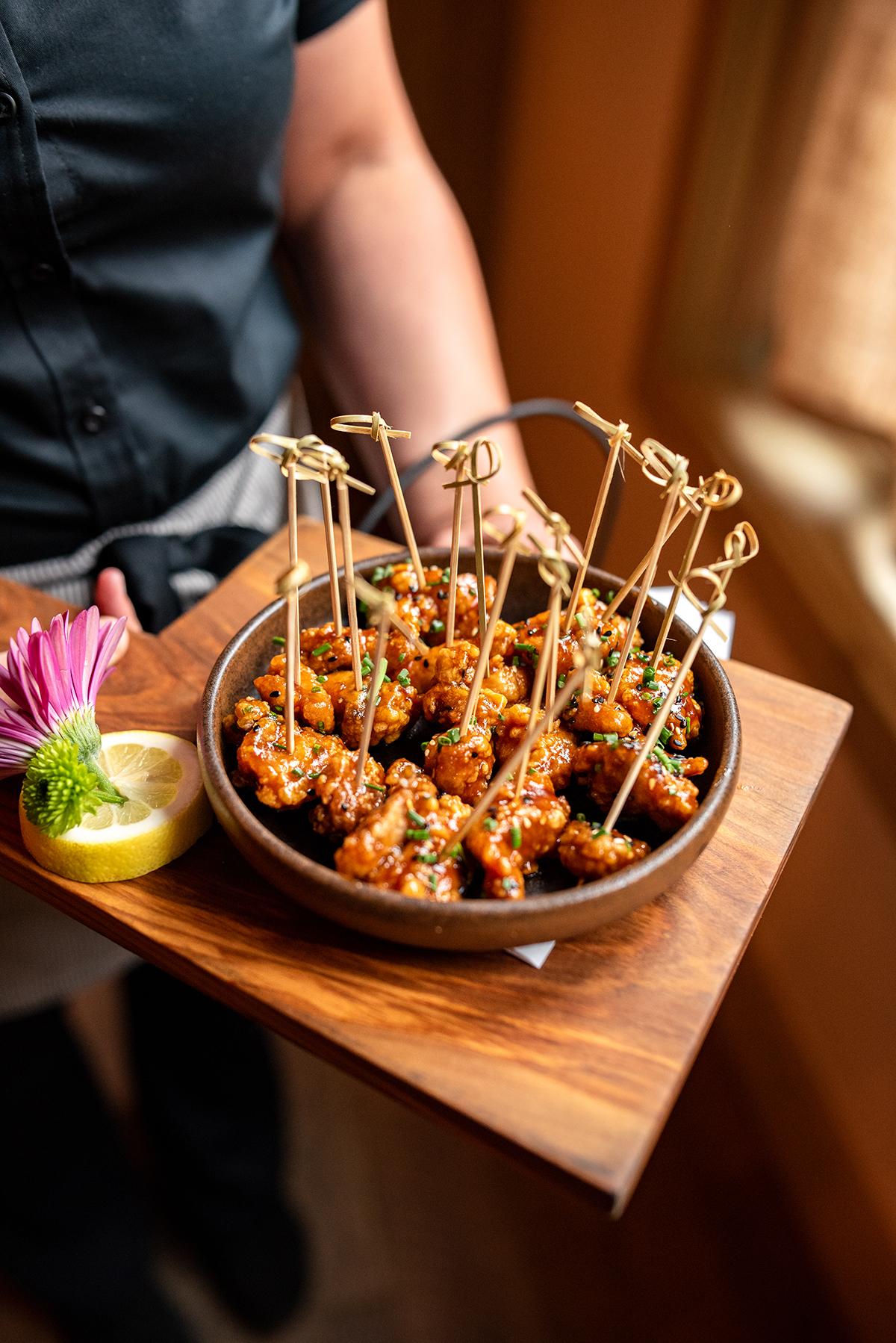 Appetizers on skewers served in a bowl on a wooden tray with garnishes.