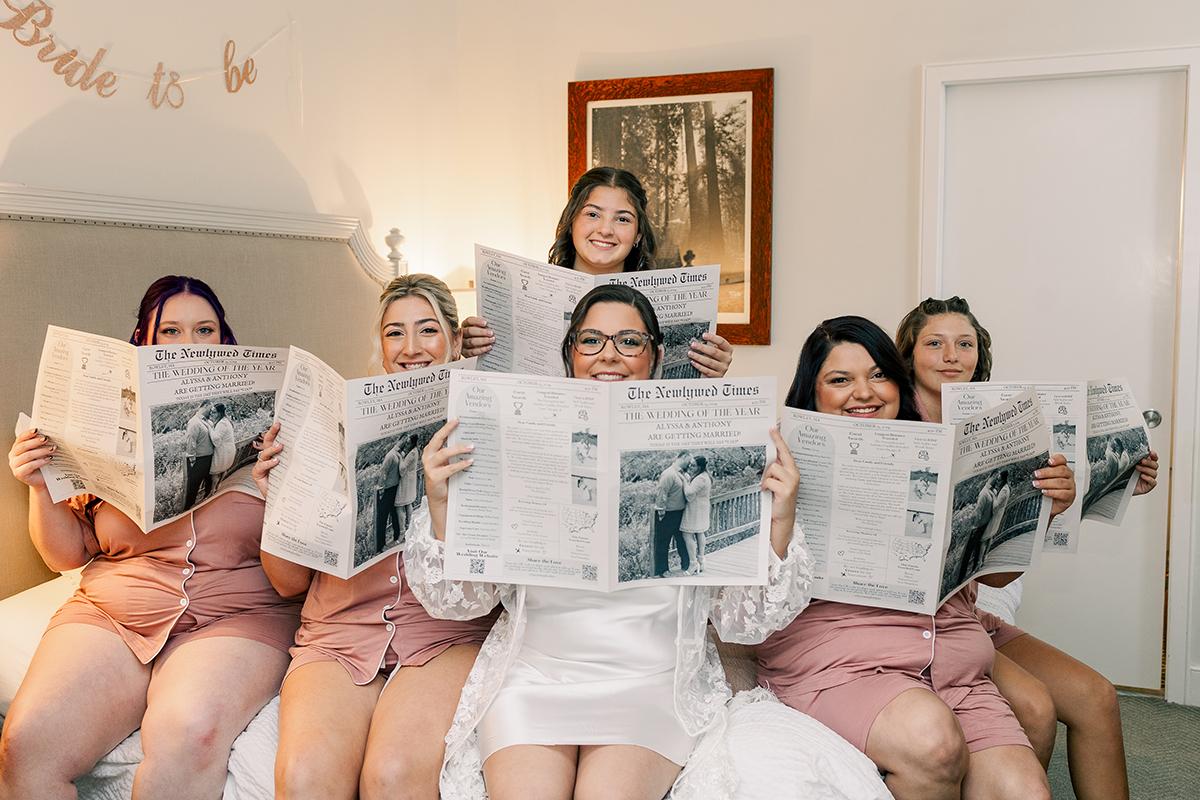 Bridal party reads newspapers on a bed, all wearing matching outfits.