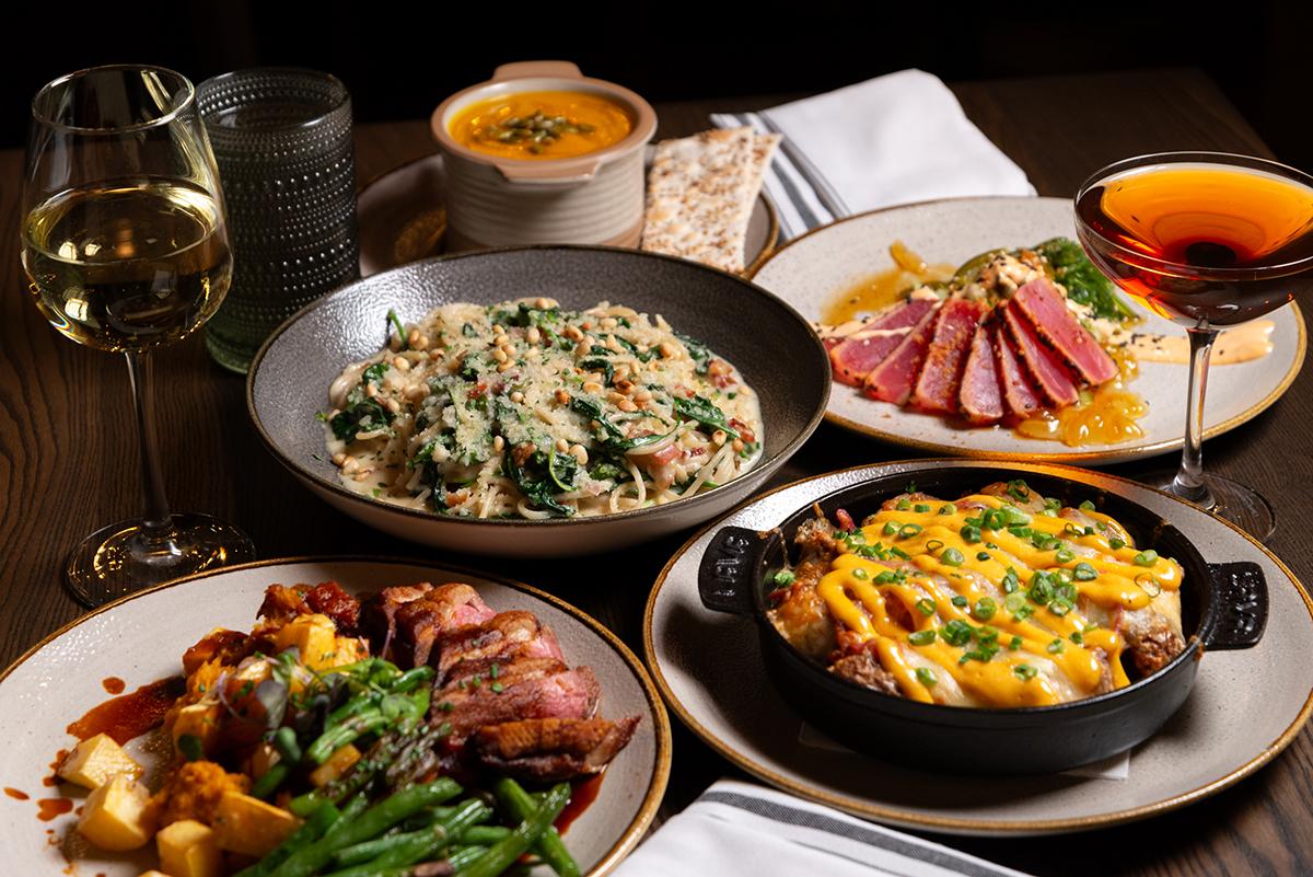 A table with various dishes, two glasses of wine, and a cocktail.