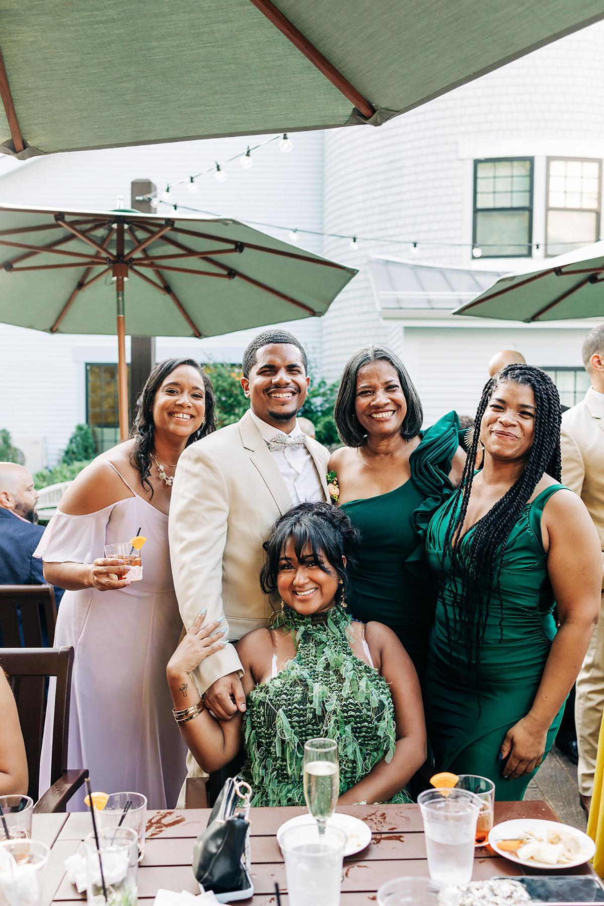 Group of people smiling at an outdoor event, with green umbrellas overhead.