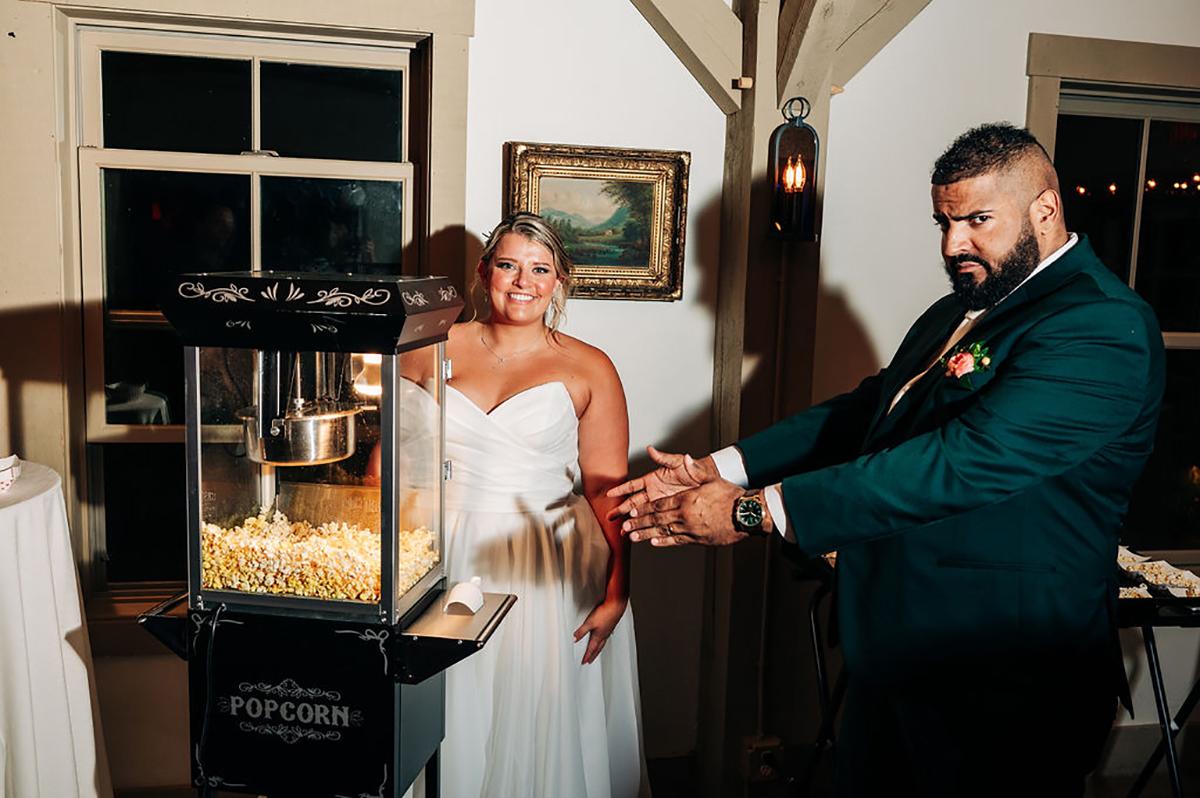 Bride and groom smiling near popcorn machine in warmly lit room.