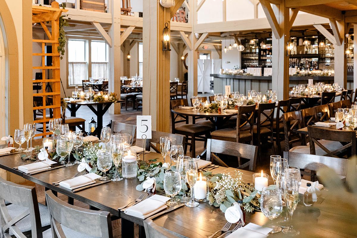 Rustic restaurant interior with elegantly set tables, candles, and wooden beams.