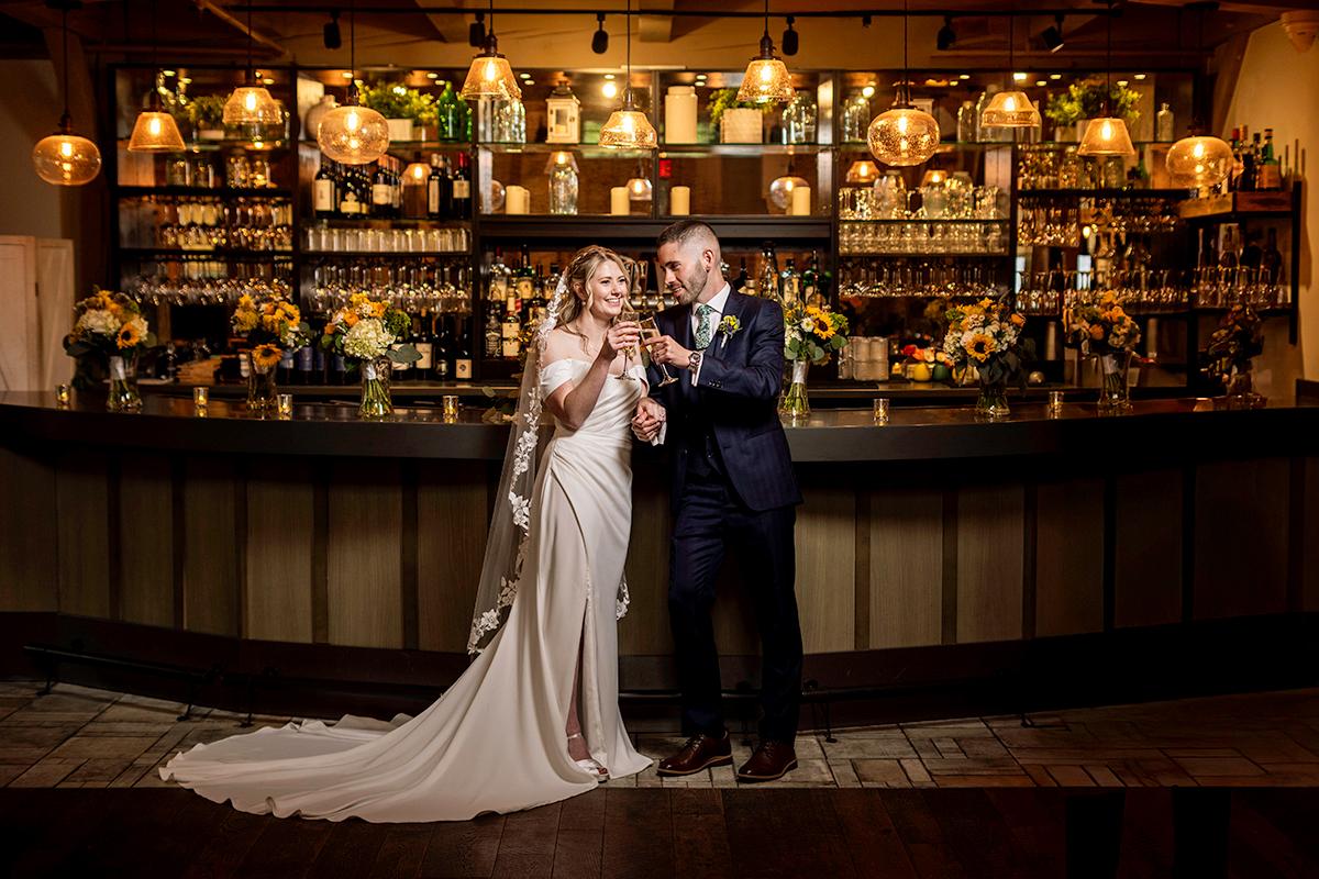 Bride and groom toast in front of a warmly lit bar.