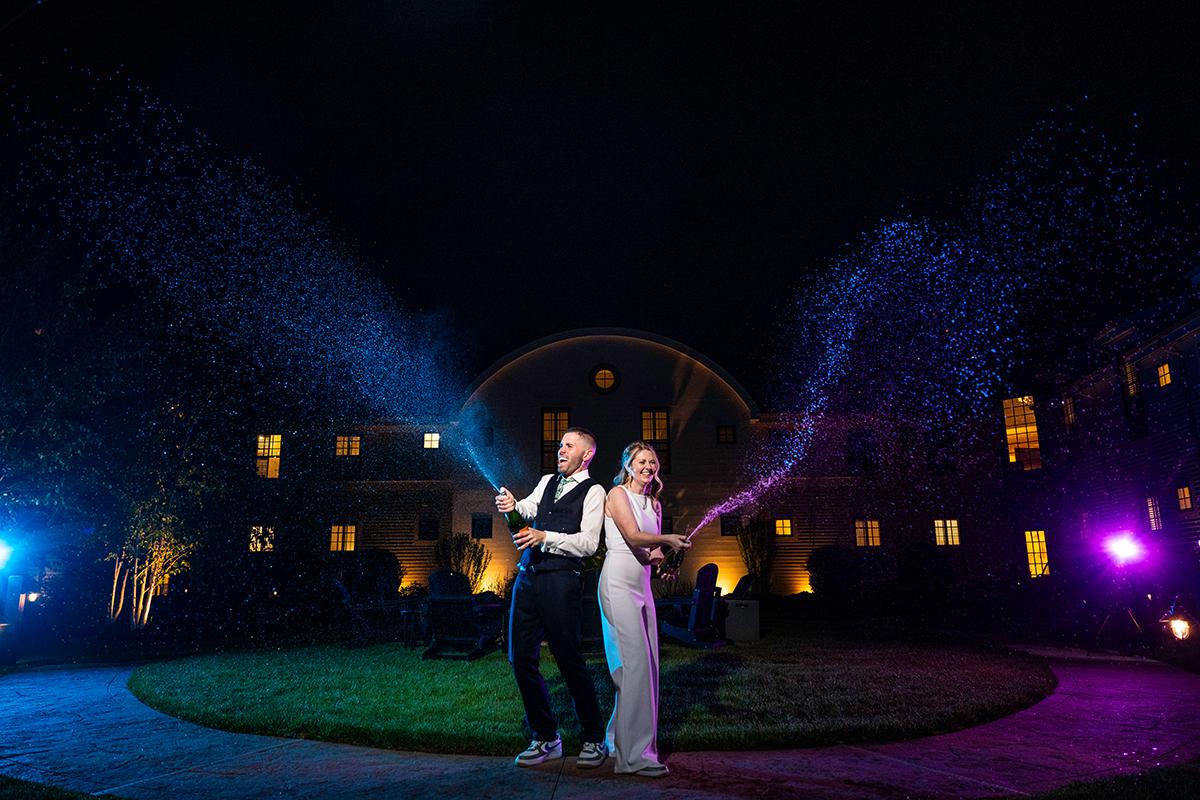Couple celebrating at night, spraying champagne with lights in the background.