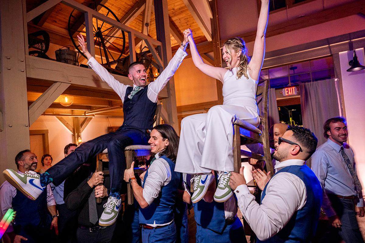 Bride and groom lifted on chairs, celebrating at a lively wedding reception.