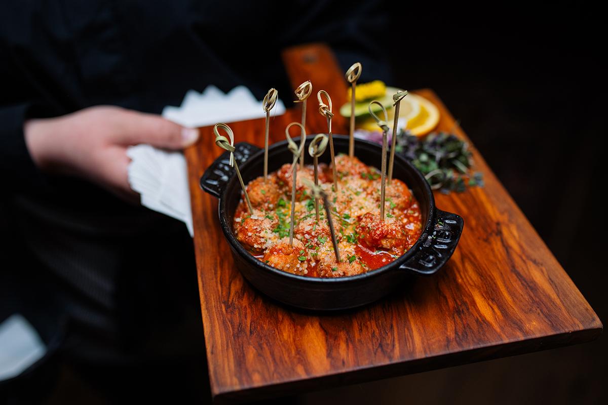 Meatballs with skewers in a black dish on a wooden serving board.
