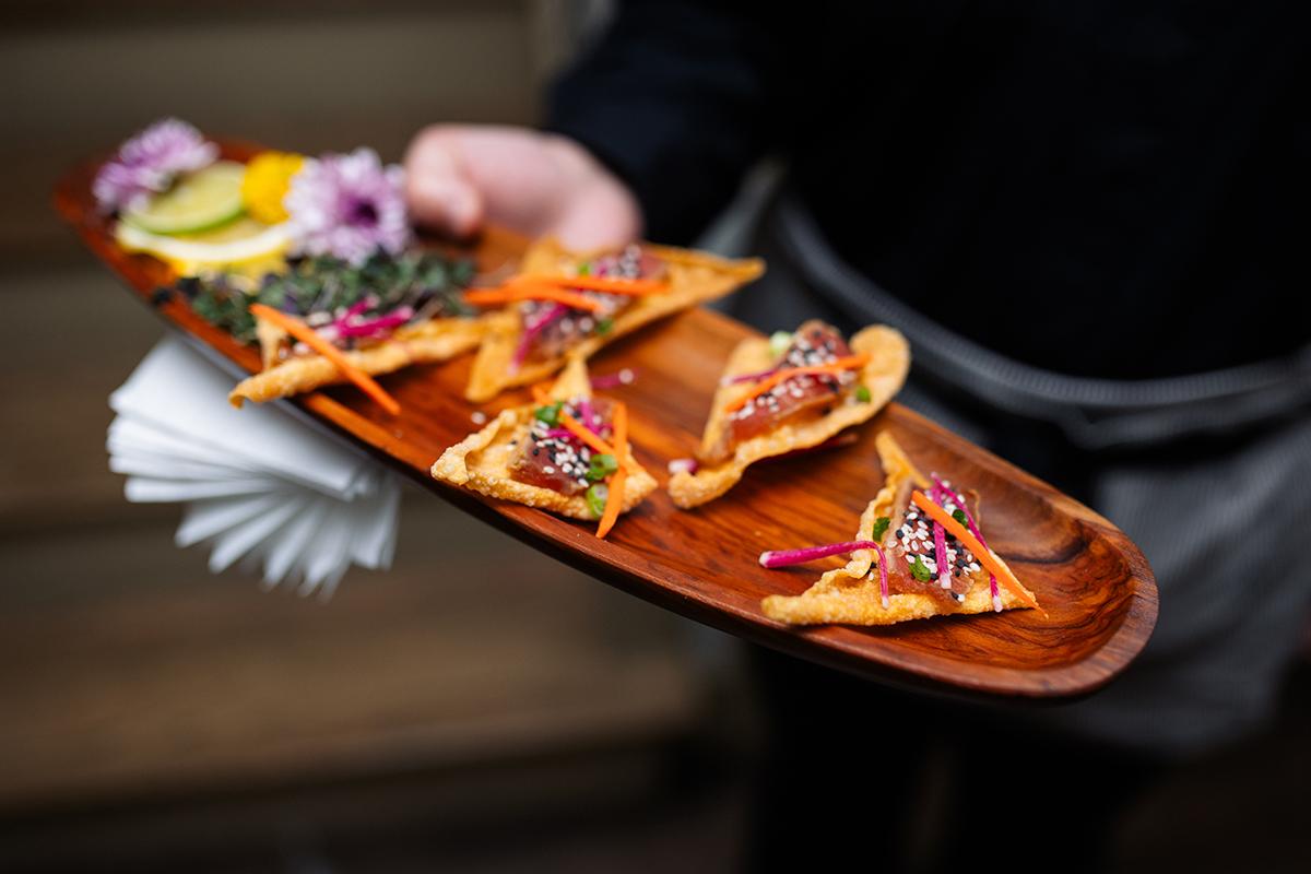 A wooden platter with gourmet appetizers and garnishes.