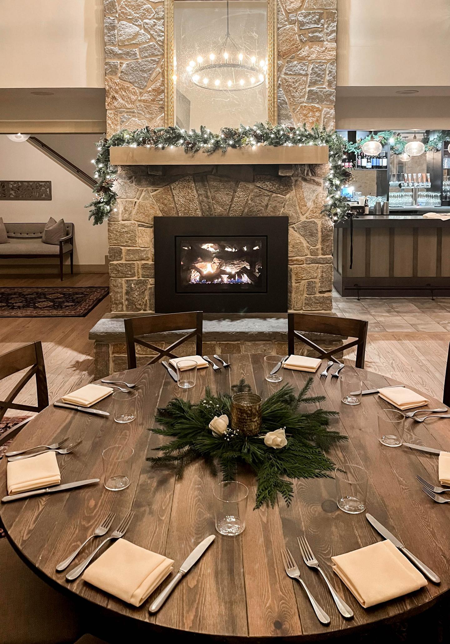 Round dining table set with flowers near a stone fireplace.