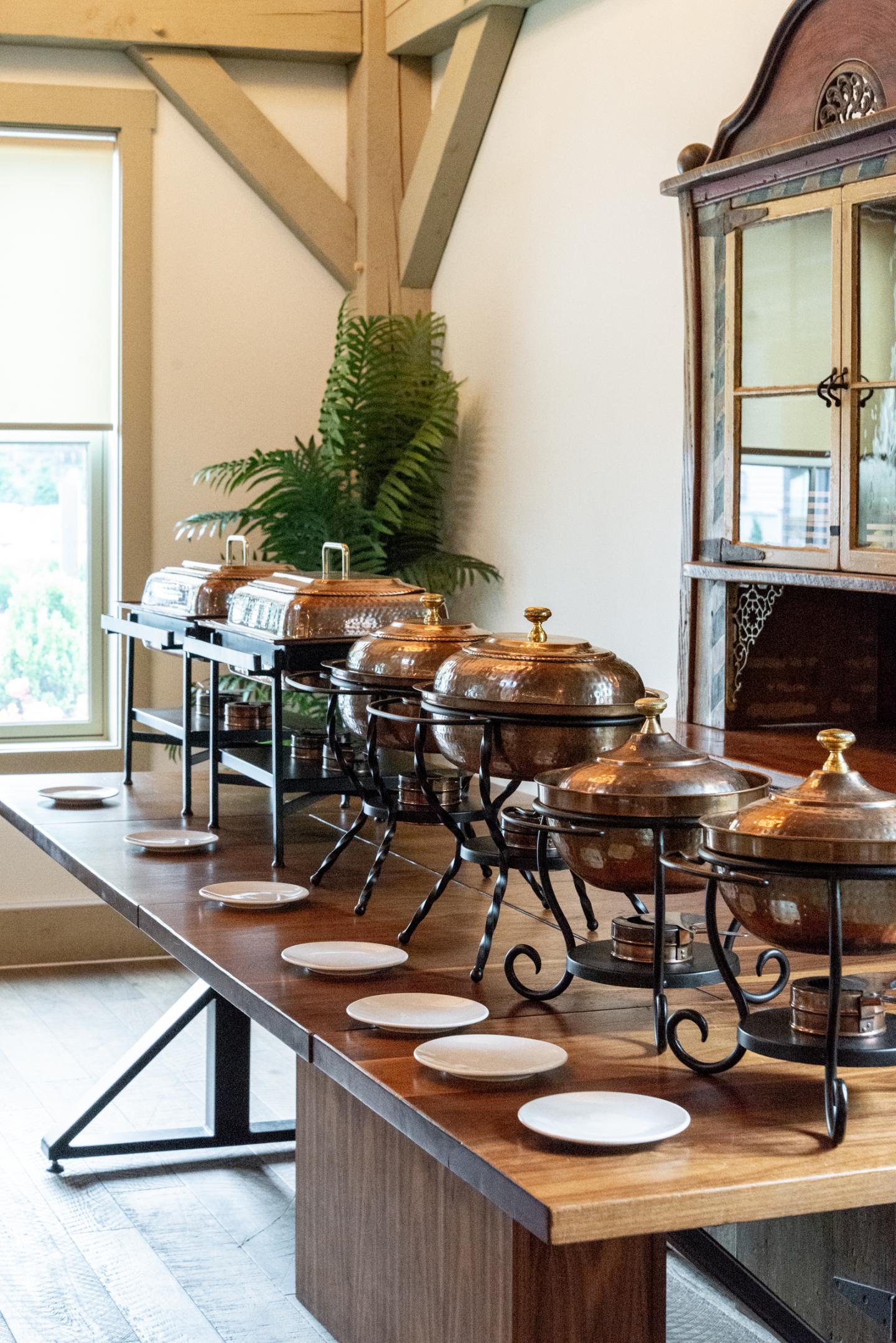 Buffet setup with covered dishes and plates on a wooden table.