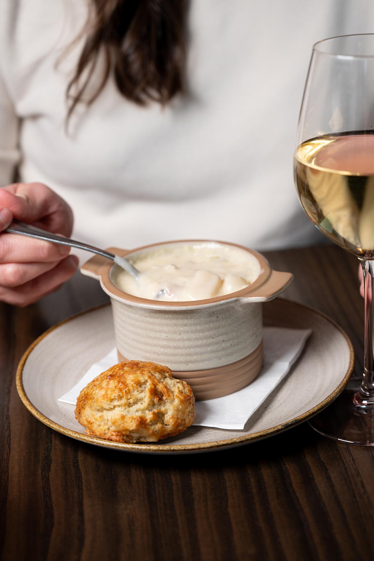 Soup in a bowl with a biscuit and a glass of white wine.