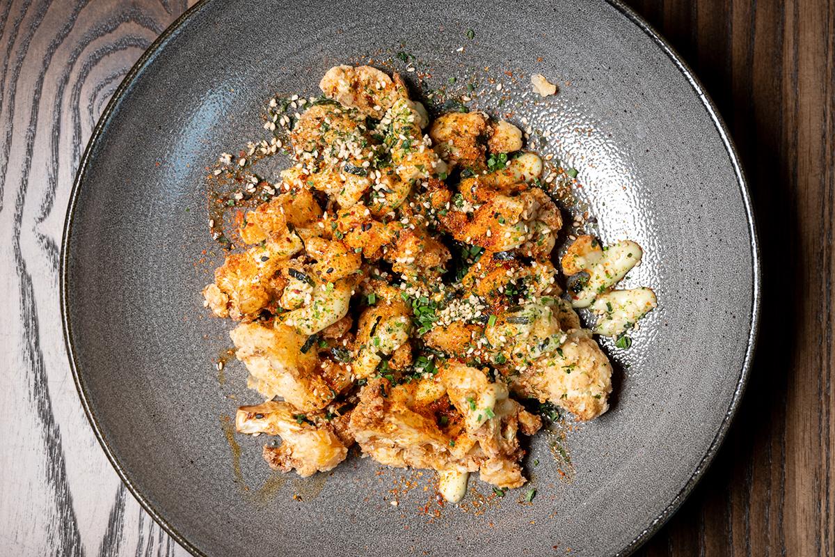 Crispy cauliflower on a grey plate, garnished with herbs and spices.
