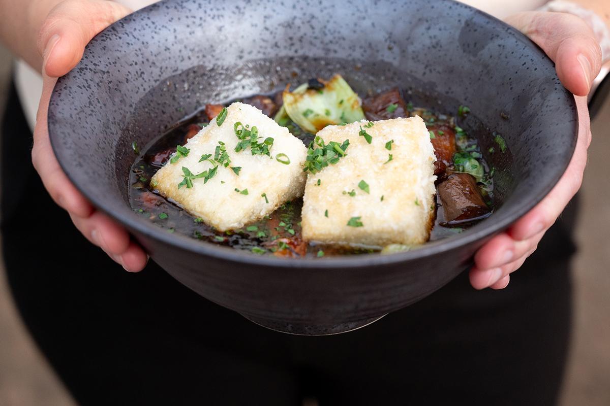 Bowl of soup with white fish and herbs, held by hands.