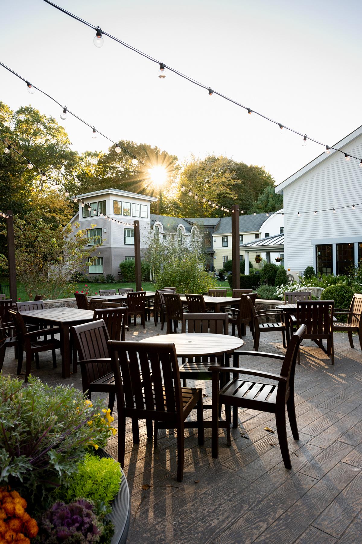 Outdoor patio with wooden tables and chairs, string lights above, sunset in the background.