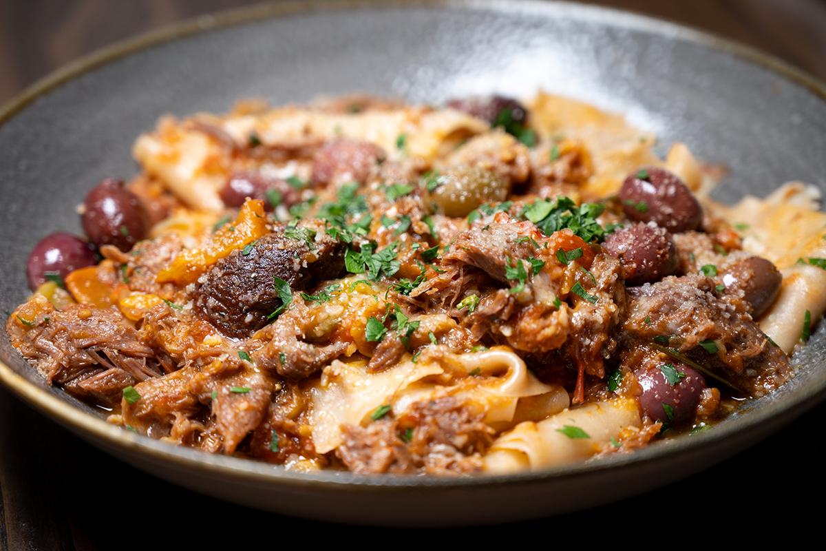 Pasta with meat sauce and olives, garnished with herbs in a dark bowl.