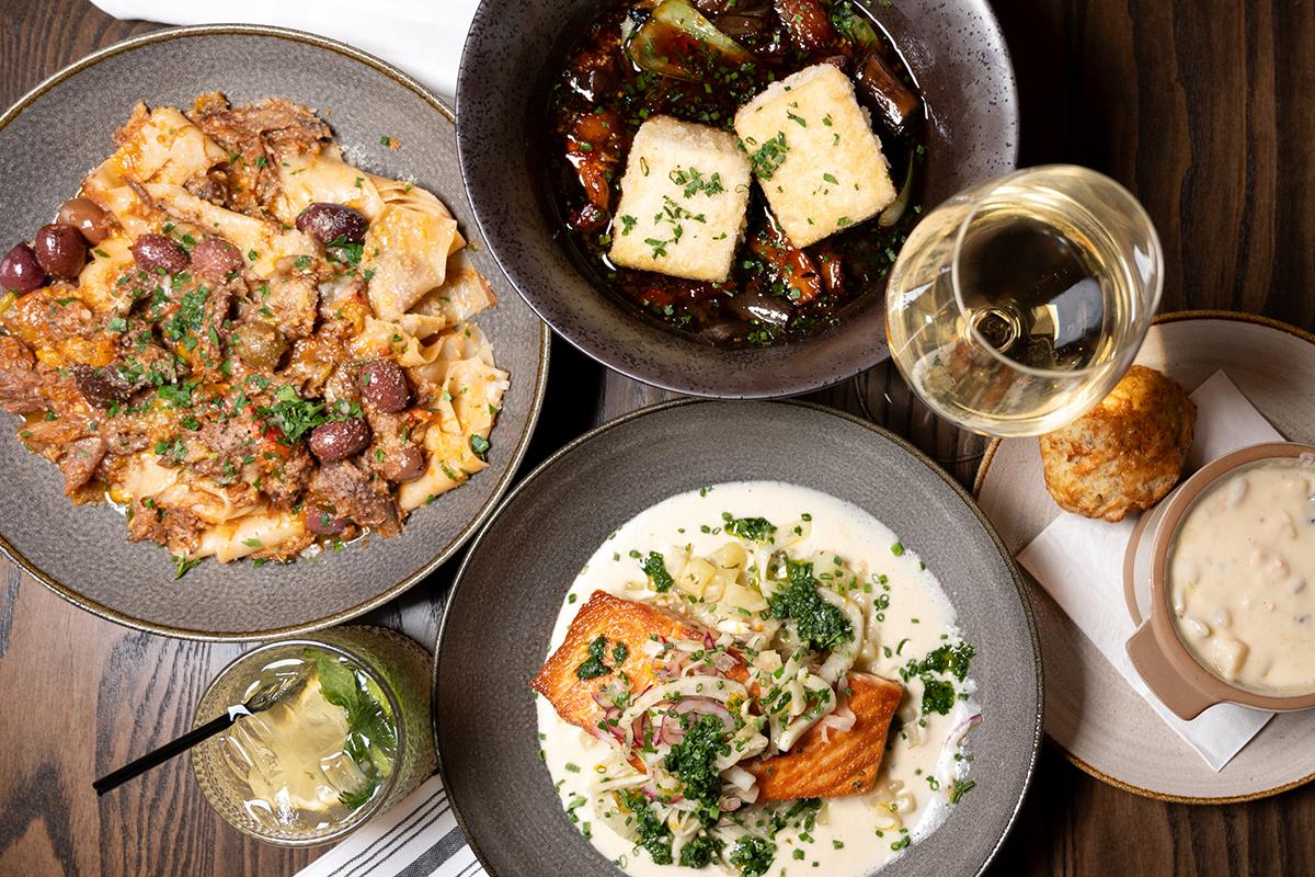Assorted dishes with fish, meat, drinks, and bread on a wooden table.