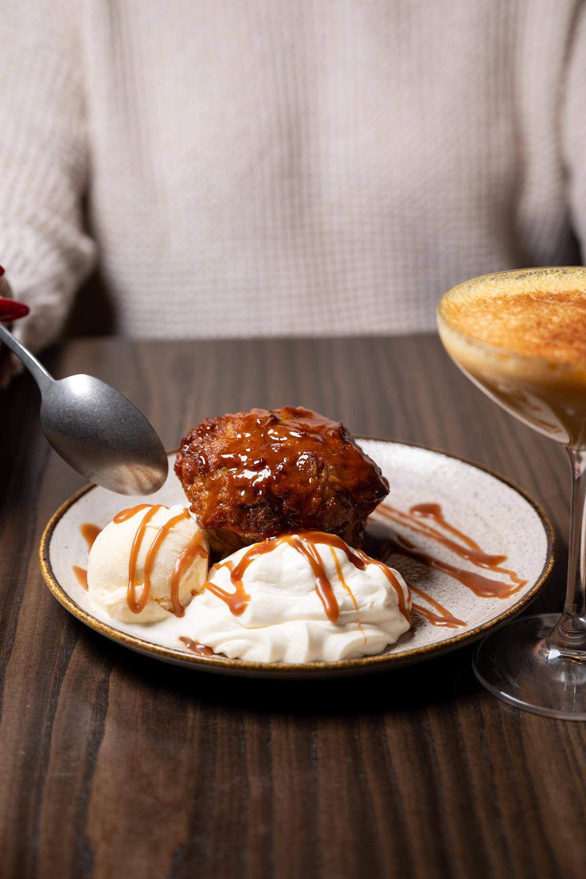 Caramel drizzled dessert with ice cream on a wooden table, next to a cocktail.
