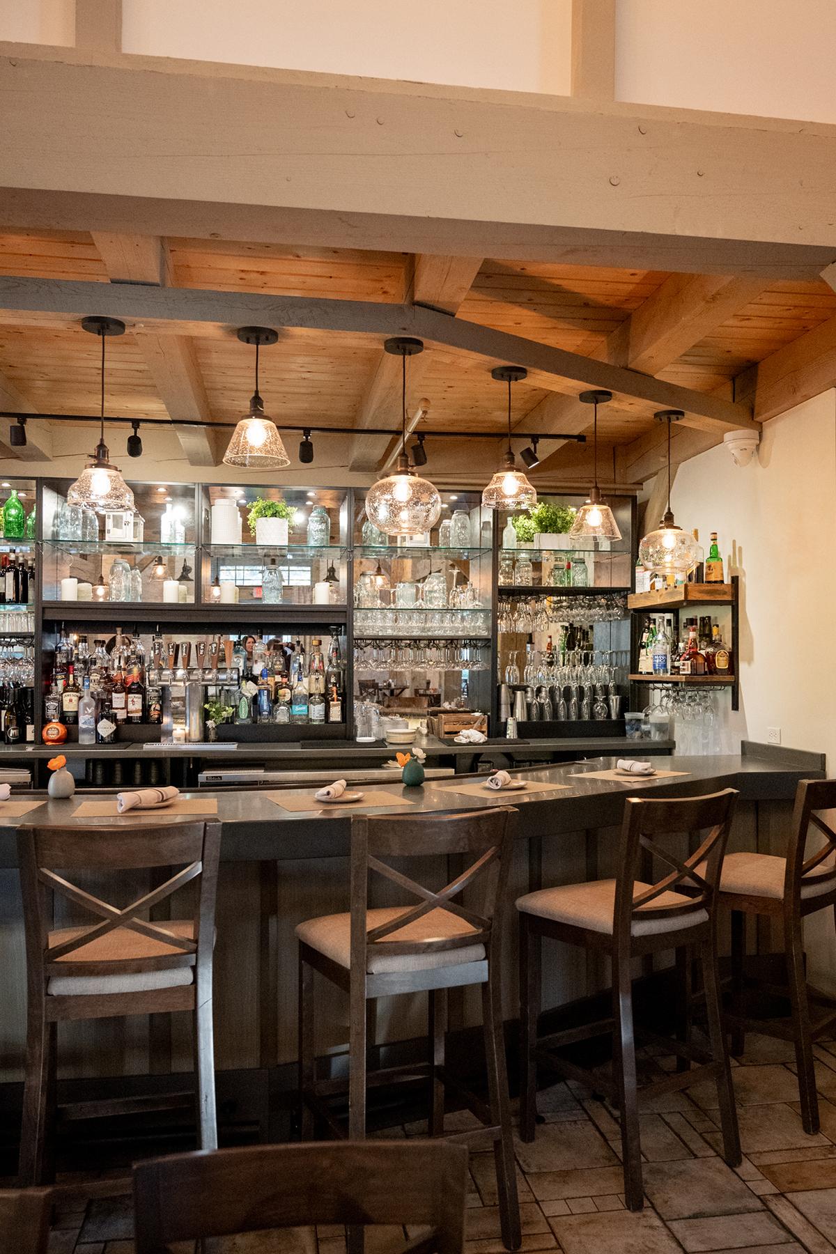 Cozy bar with wooden stools, bottles, and hanging lights.