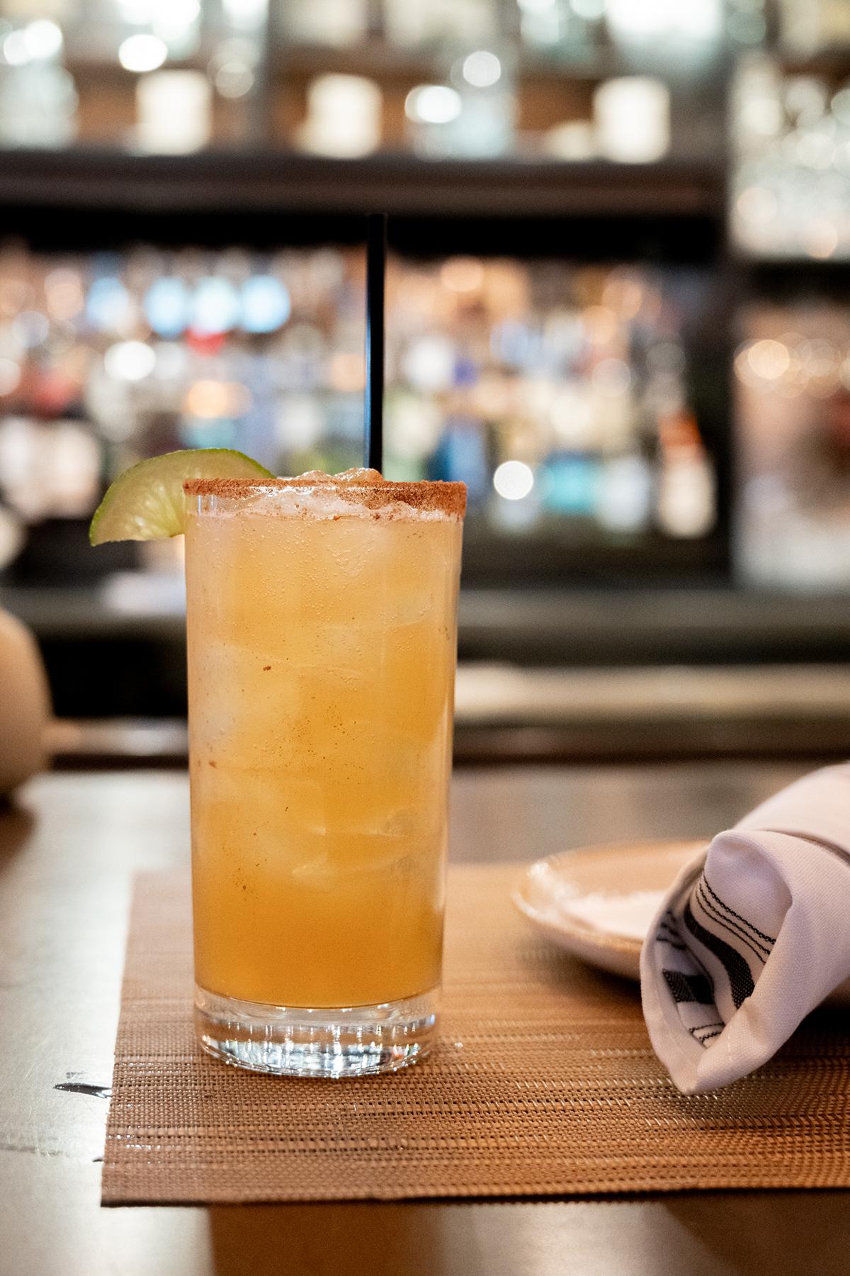 Tall cocktail with lime slice, straw, and salted rim on a bar mat.