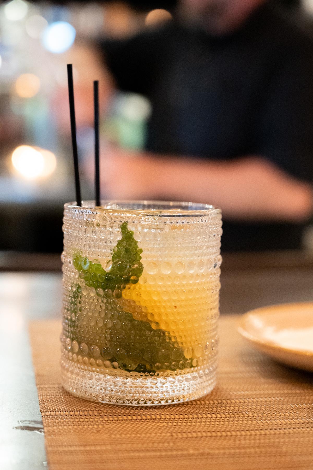 A cocktail with lime and mint in a textured glass with two straws.