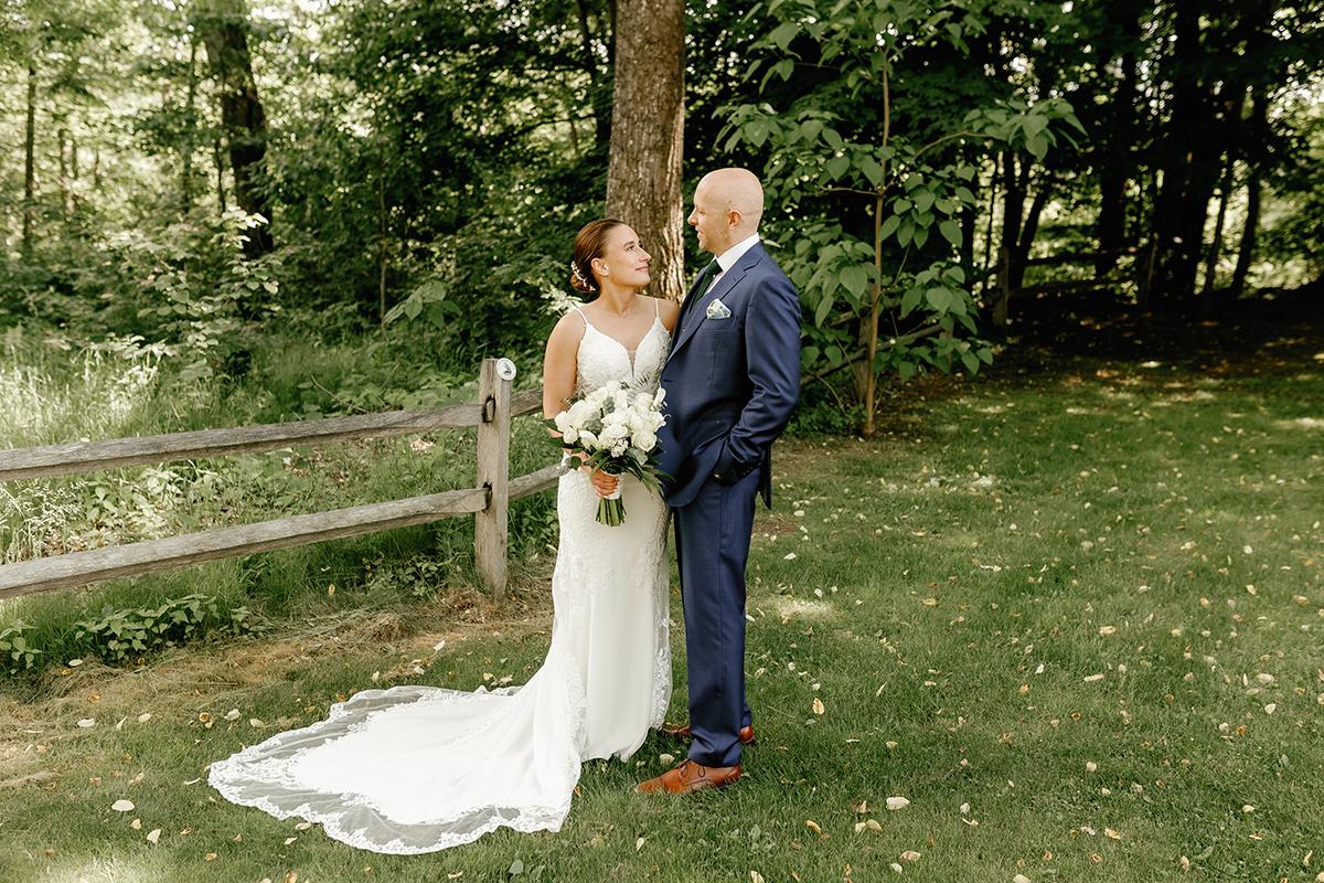 Bride and groom stand in a garden, smiling at each other.