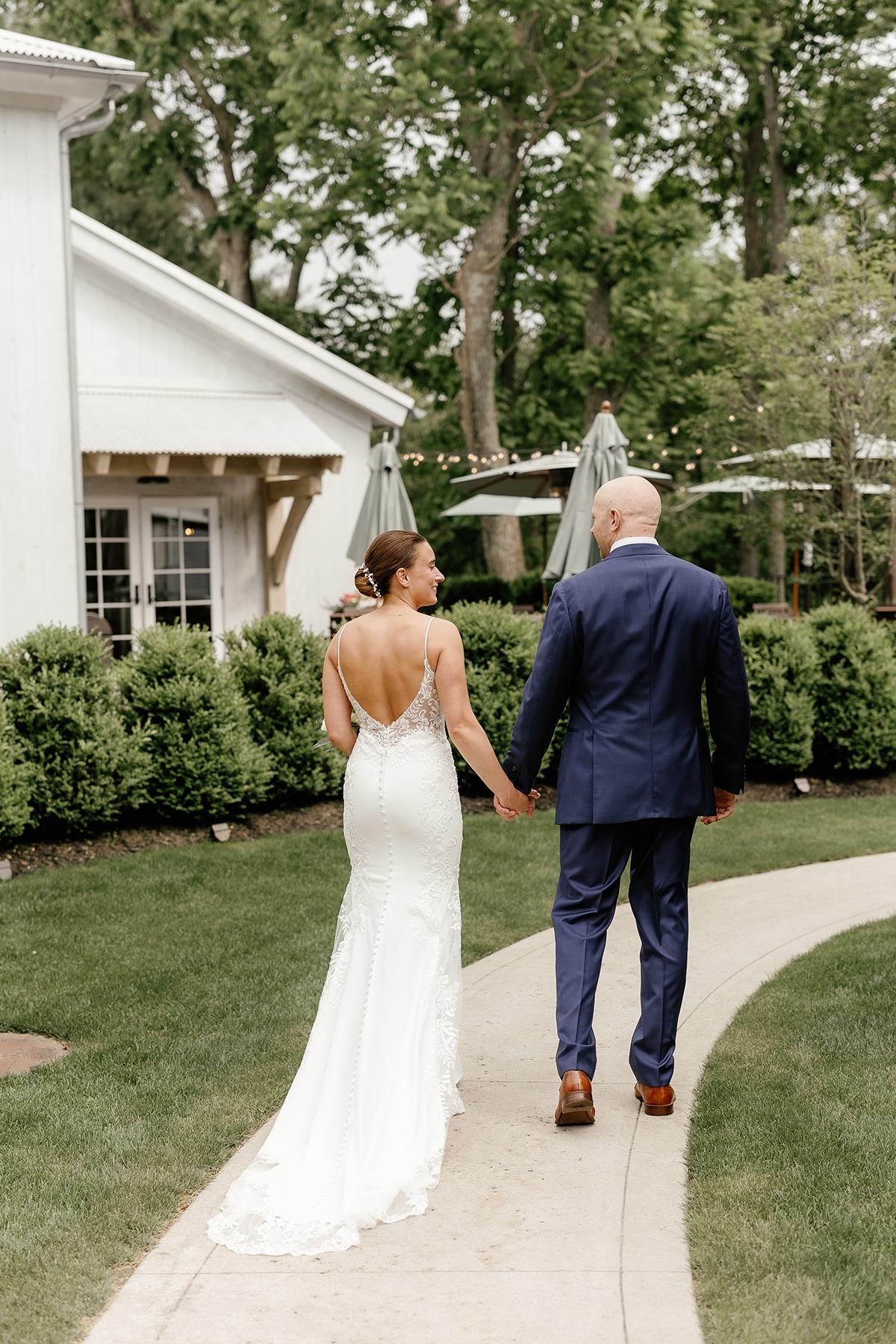 Couple walking hand in hand on a garden path in formal attire.
