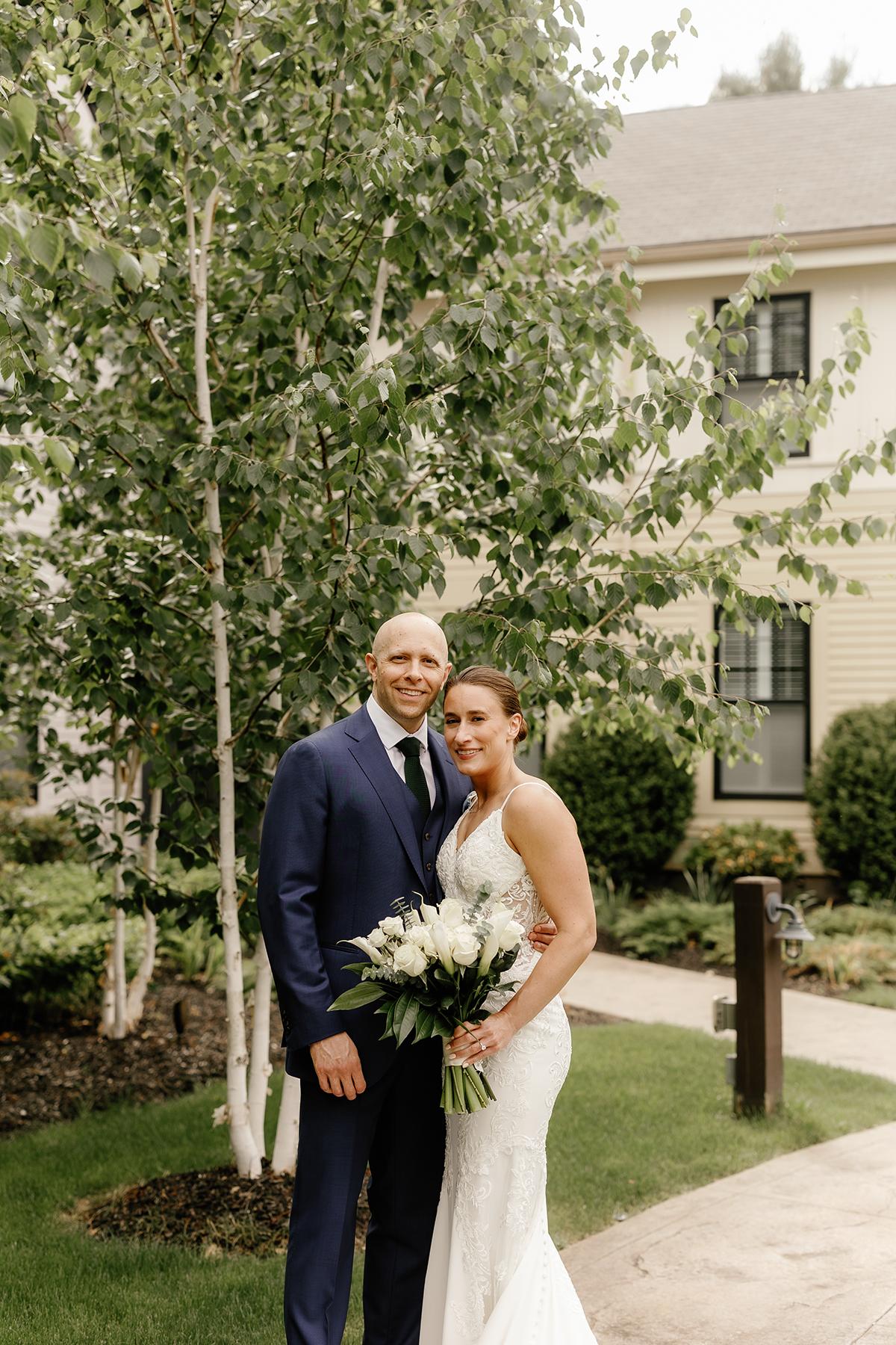 Couple in wedding attire smiling in a garden setting.