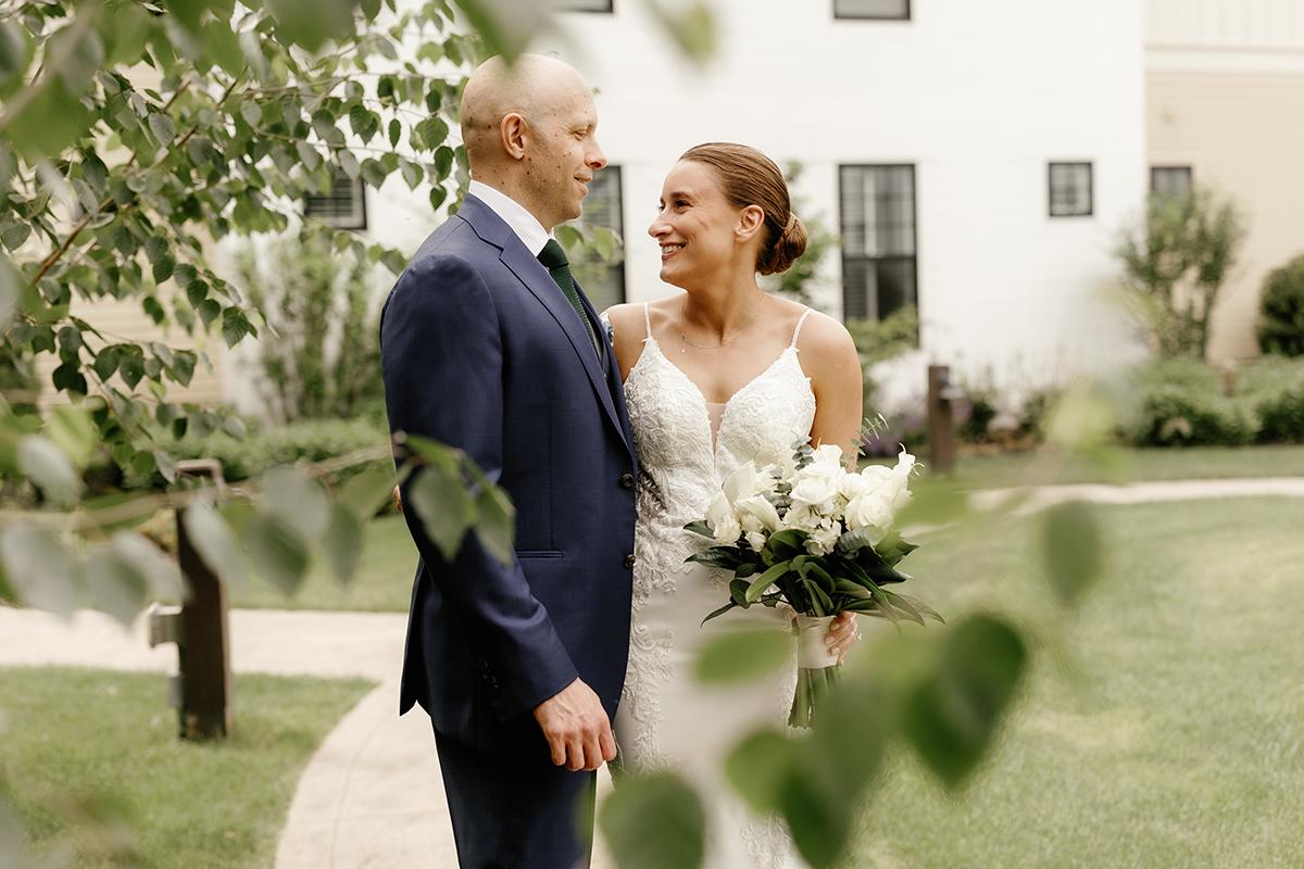 Bride and groom smiling at each other in a garden.