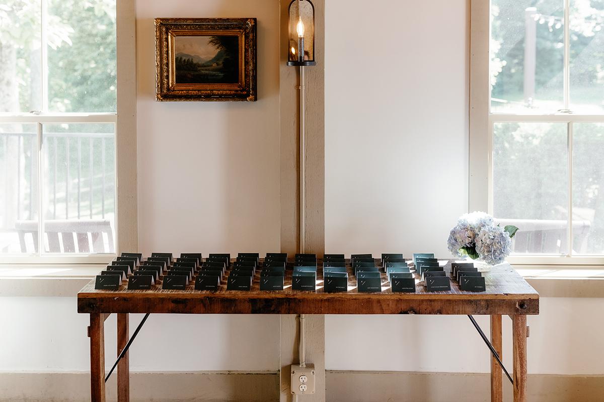 Wooden table with multiple phones in a room with two windows and a small painting.