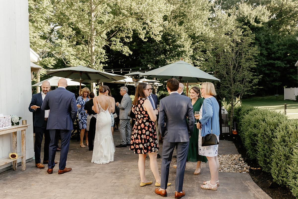 Outdoor wedding reception, guests mingling under umbrellas on patio.