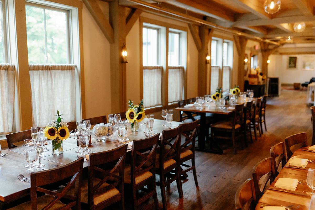Elegant dining room with long tables, sunflowers, and soft lighting.